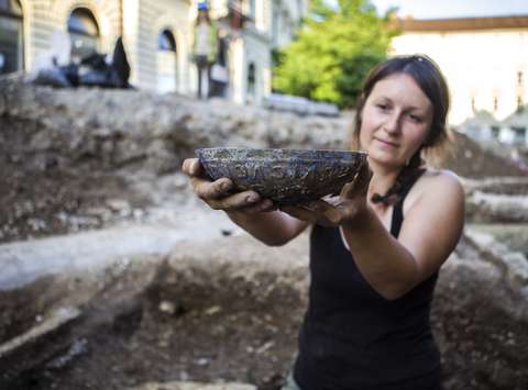 Steklena posoda z v visokem reliefu izdelanem okrasu in zdravico izpisano v grščini. Posoda je pripadala pokojnici, pokopani v osrednjem sarkofagu na grobišču znotraj kasnejše pokopališke cerkve.